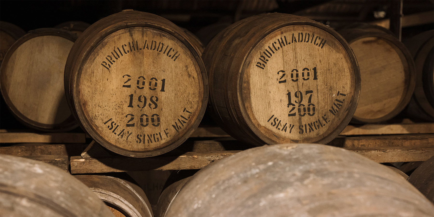 Close-up of Bruichladdich Distillery whisky casks stamped with '2001 Islay Single Malt', resting in a bonded warehouse.